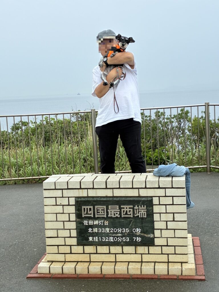 「四国最西端 佐田岬灯台」と刻まれた碑と、犬を抱いた人物