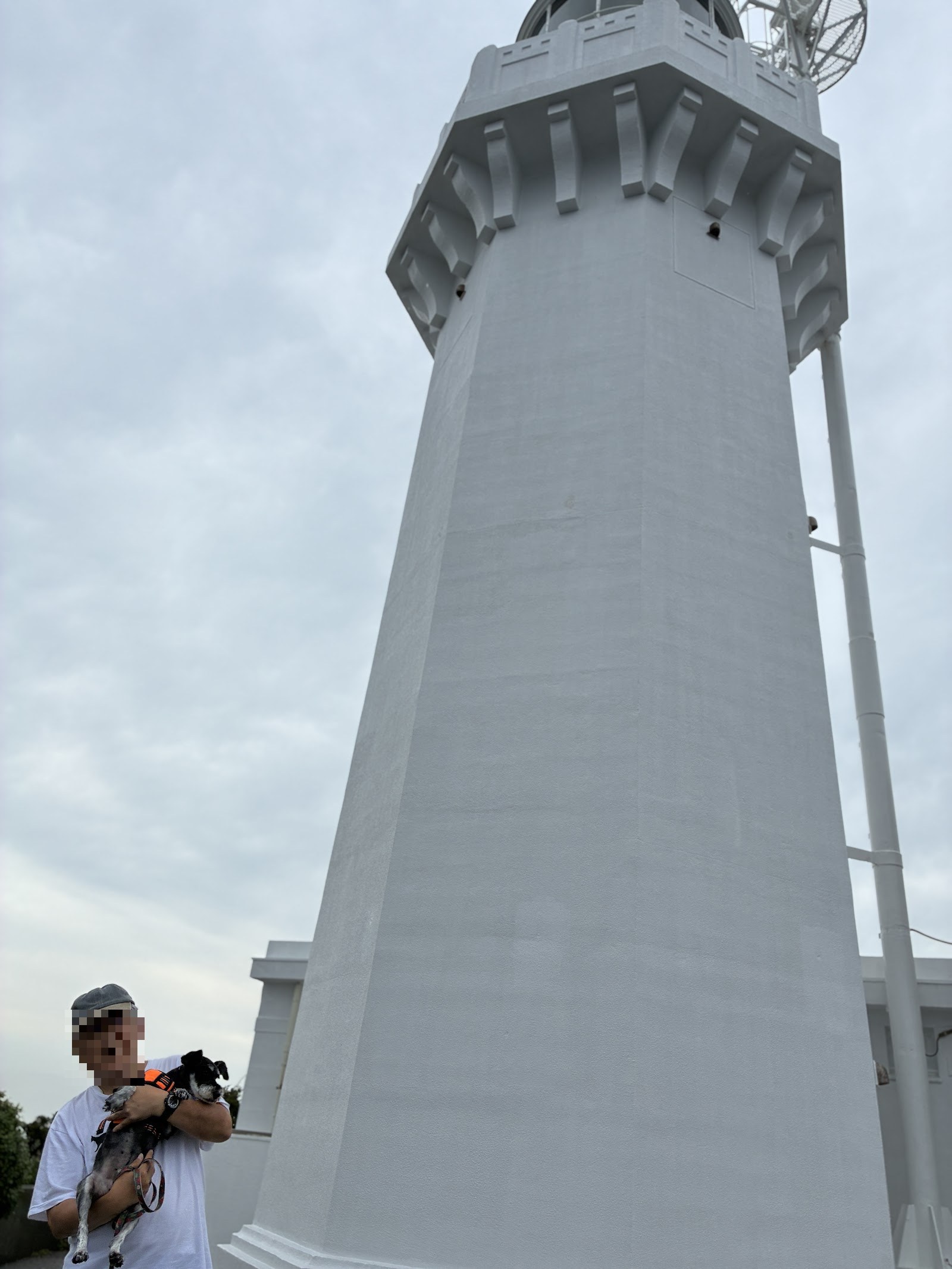 下から見上げた佐田岬灯台の全景。手前に犬を抱いた人