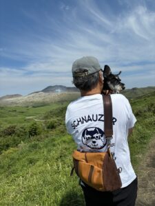 犬を肩に抱いて噴煙の上がる山を見る人の後ろ姿