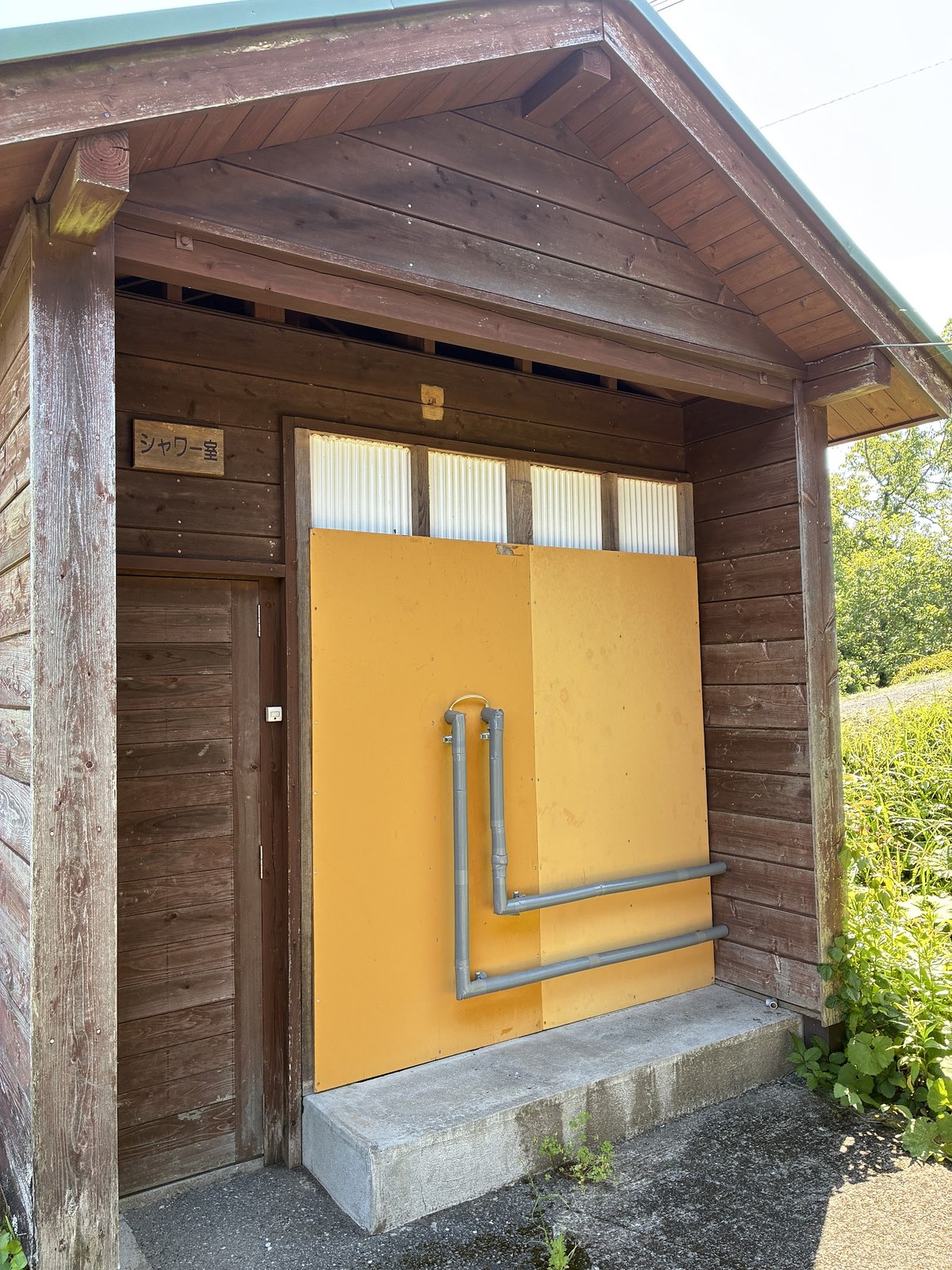 木造の建物に取り付けられた黄色い扉のシャワー室