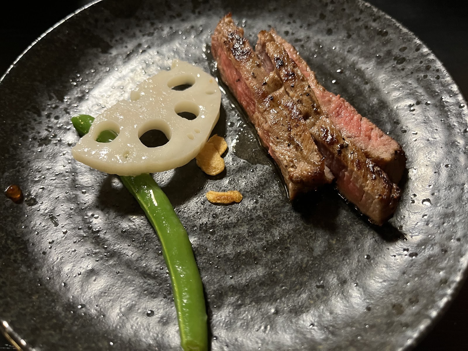 黒い皿に盛られた焼いた牛肉とれんこん