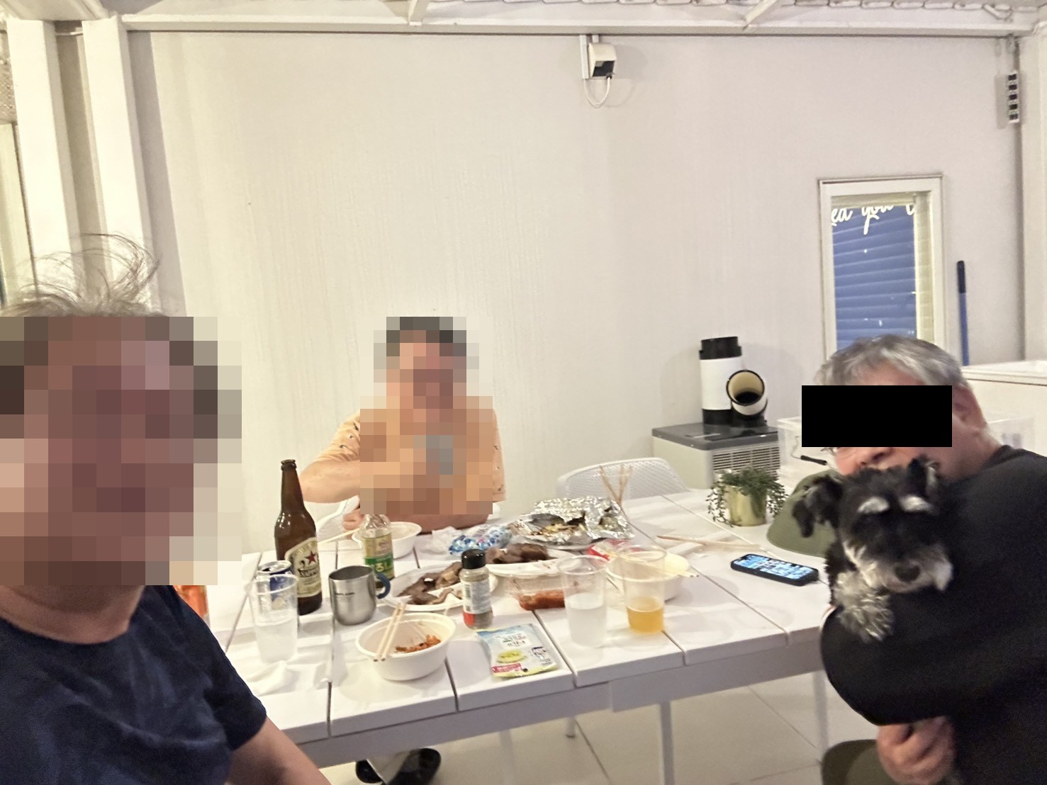夜のパティオで食卓を囲む3人と、抱かれているミニチュアシュナウザーのトリコ